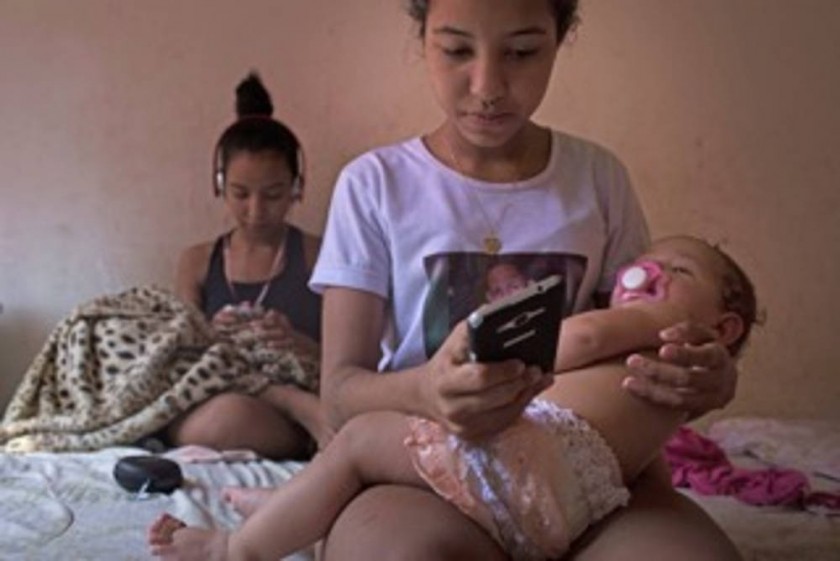 Nayane, de 15 años, sostiene en brazos a su hija Ana Sophia, de 10 meses, mientras manda mensajes con el celular.