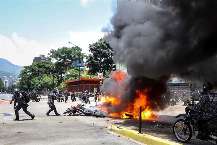 Agentes de la Guardia Nacional Bolivariana lanzan motocicletas usadas por periodistas a incendio causado por explosión.