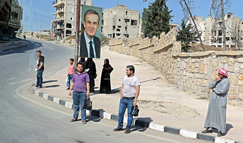 RESTITUCIÓN. Residentes de una ciudad siria esperan el autobús en una calle bajo el retrato del ex presidente sirio...
