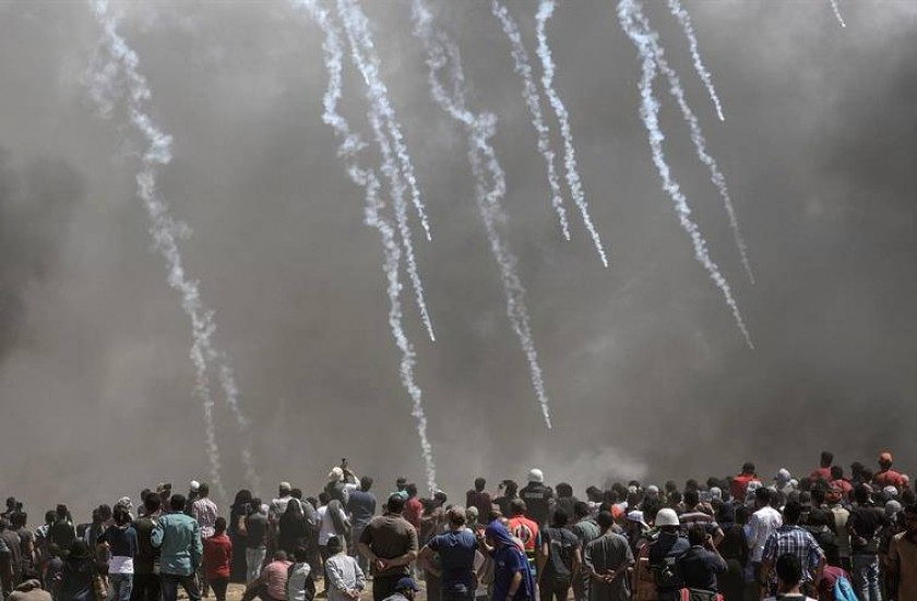 Varios manifestantes palestinos ante un muro de gas lacrimógeno tras las protestas convocadas cerca de la frontera. EFE
