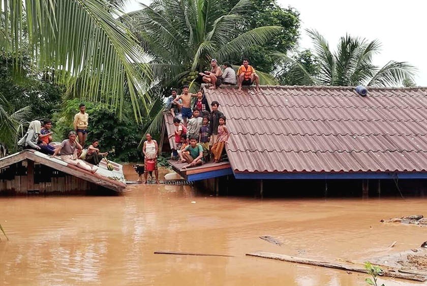 Un grupo de personas aguarda en lo alto de un tejado en una zona inundada tras el derrumbe de una presa hidroeléctrica.