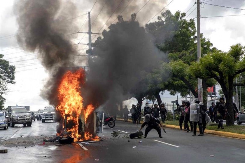 Integrantes de la Policía de Nicaragua patrullan frente a un vehículo policial que se quemó el domingo. EFE
