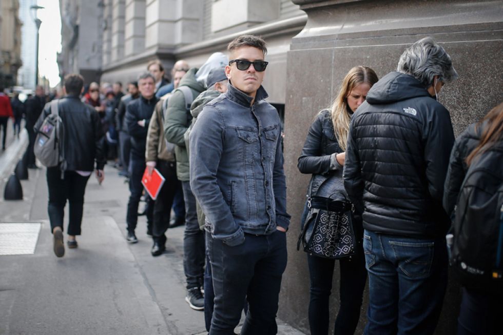 REACCIÓN. Clientes hacen filas en bancos esperando el inicio de la jornada bursátil para retirar dinero en efectivo ayer, lunes.