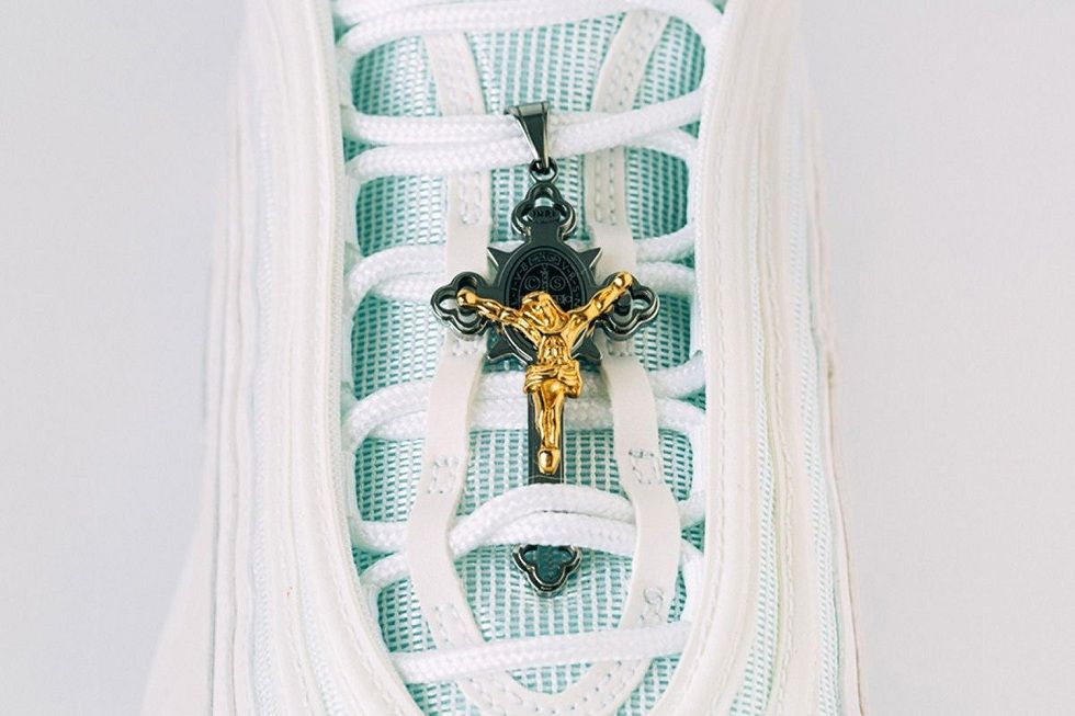 Fotografía cedida por el estudio de diseño MSCHF donde se muestra el lado frontal de las "Zapatillas de Jesús", con un crucifijo dorado de Jesús en los cordones.