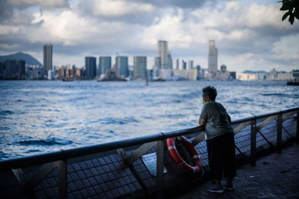 Una anciana usa mascarilla mientras está de pie junto a una barrera a lo largo del puerto Victoria en Hong Kong.