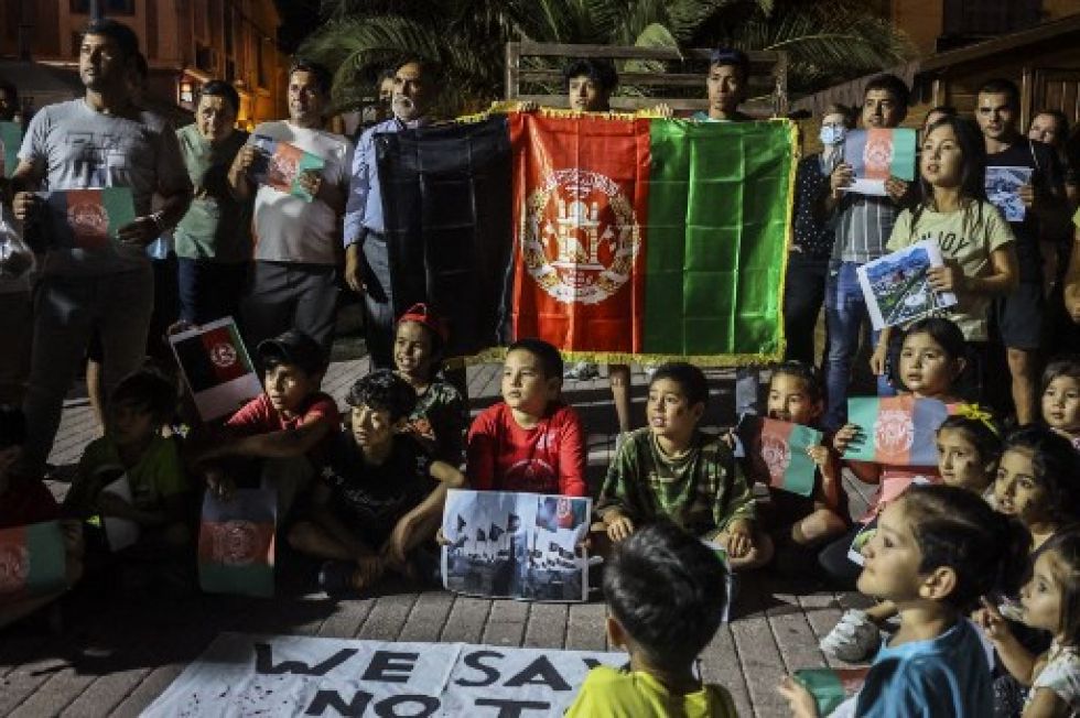 Migrantes afganos sostienen la bandera afgana mientras protestan por la toma de posesión de Afganistán por los talibanes, en la isla de Lesbos.