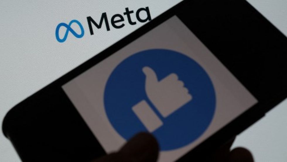 Foto ilustrativa muestra a una persona que usa Facebook en un teléfono inteligente frente a una pantalla de computadora que muestra el logotipo de Meta.