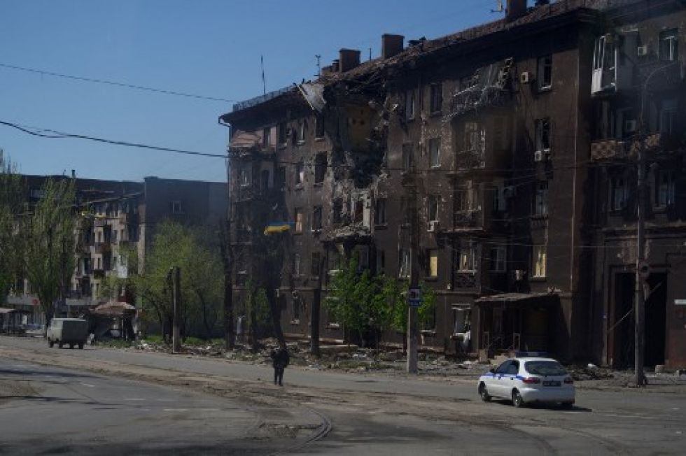 Una persona camina por una calle frente a un edificio residencial carbonizado en la ciudad de Mariupol.