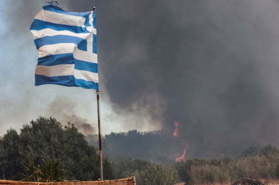 Una bandera de Grecia con el humo de fondo de un incendio forestal que se acerca al centro turístico costero de Vatera en la isla oriental de Lesbos, el 23 de julio.