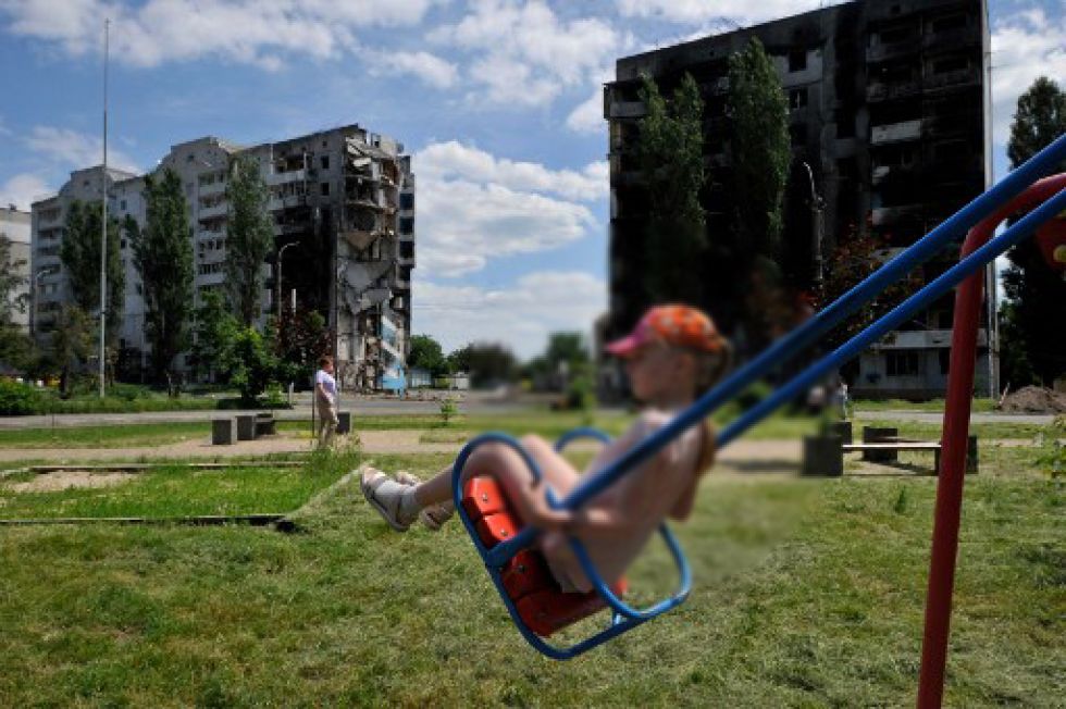 Imagen referencial. Una niña juega al columpio frente a un edificio colpasado por los ataques rusos.