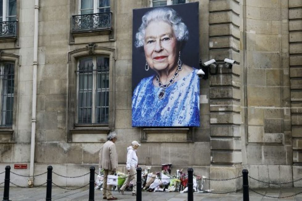 Patones pasan frente a un retrato de la reina Isabel II, donde se dejaron flores en la embajada británica en París.