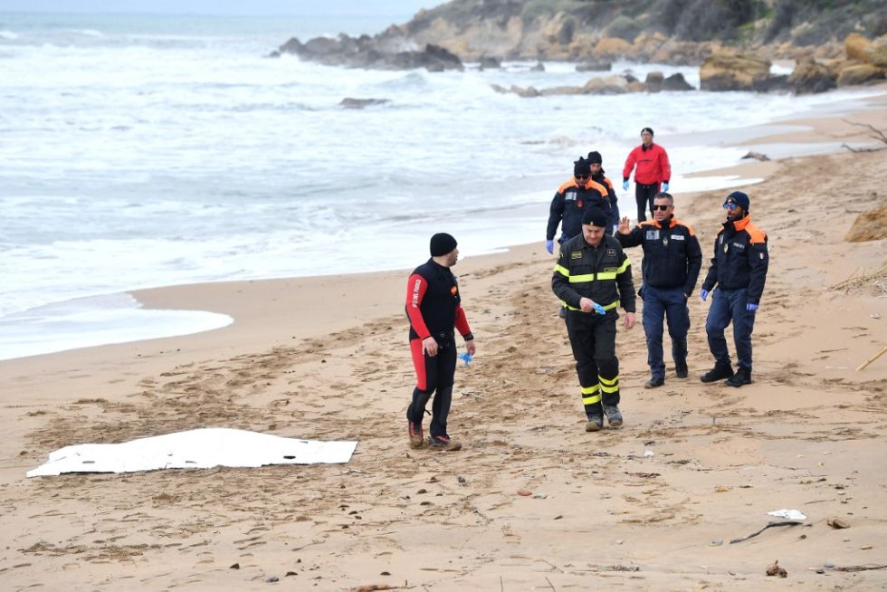 El oficial de la Guardia Costera italiana y los buzos del Cuerpo de Bomberos se paran cerca del cuerpo de un migrante muerto