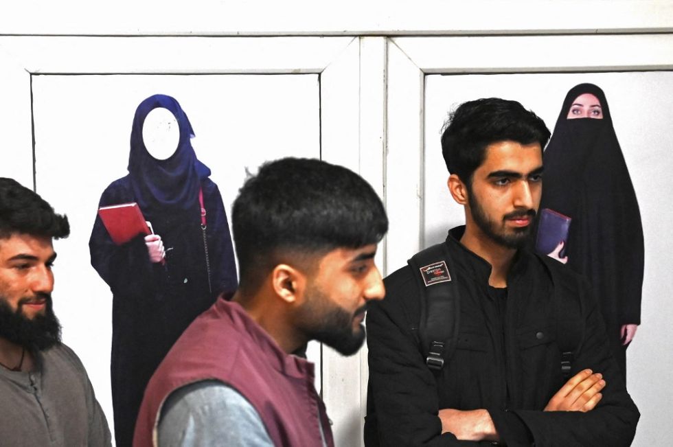 Los estudiantes varones se paran frente a un cartel que ordena a las mujeres que se cubran con un hiyab, en el pasillo de una universidad privada