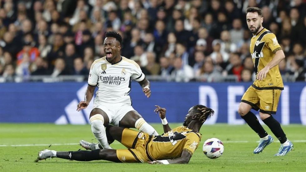 El delantero brasileño del Real Madrid Vinícius Júnior (i) disputa una posesión ante Pathe Ciss (suelo) defensa senegalés del Rayo Vallecano.