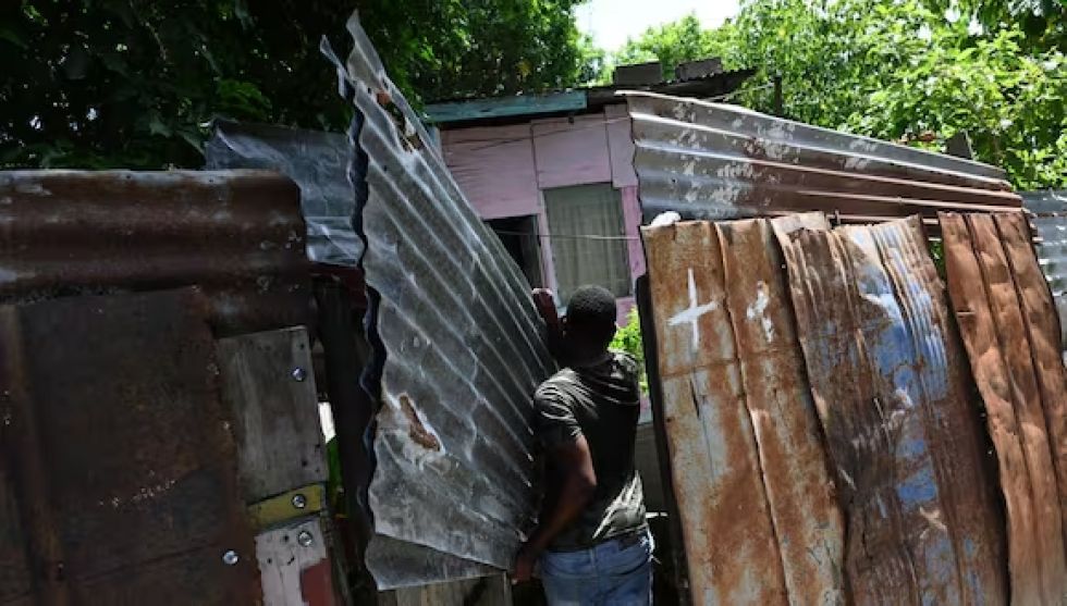 Un hombre lleva laminas de zinc para proteger el techo y las ventanas de su casa ante la inminente llegada del huracán Beryl.