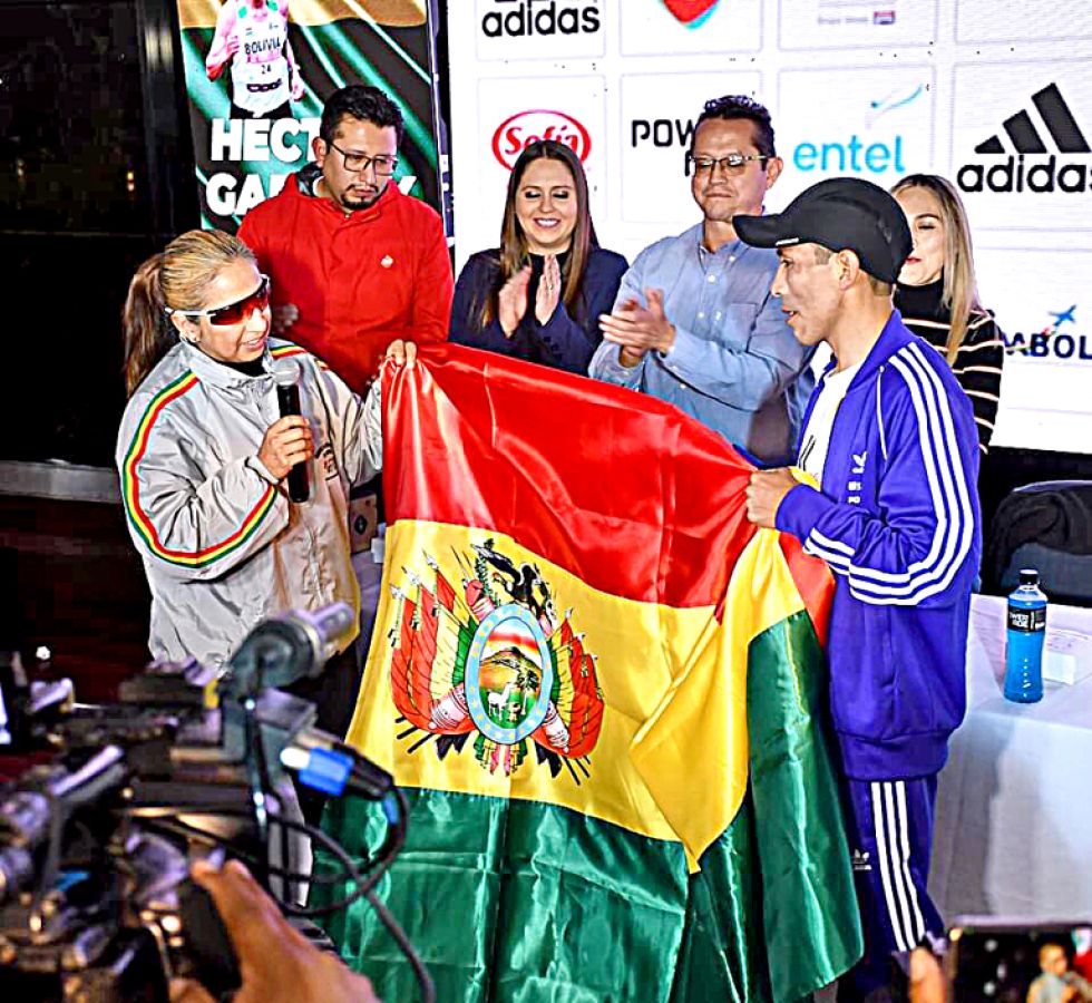 El fondista orureño recibió la bandera boliviana de la mano de la exmarchista Geovana Irusta.