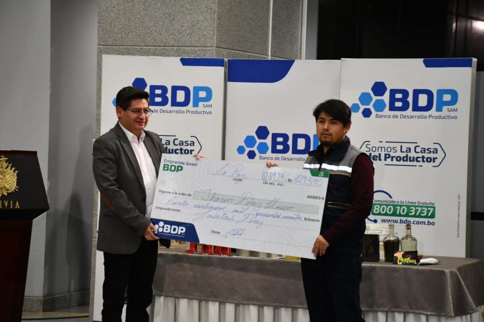 El ministro de Economía, Marcelo Montenegro (i), entrega un cheque simbólico a un joven emprendedor.