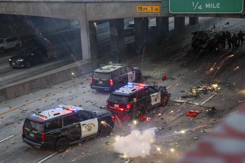 Agentes de policía se refugian mientras activistas lanzan piedras y fuegos artificiales sobre sus vehículos durante las protestas en Los Ángeles.