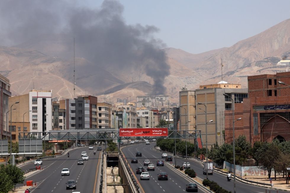 Vehículos circulan por una autopista mientras se eleva humo al fondo desde una refinería de petróleo, al noroeste de Teherán, Irán.